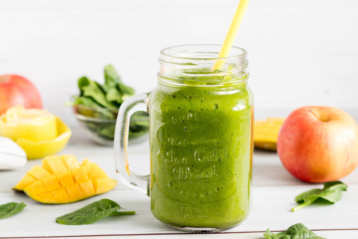 spinach mango apple smoothie in a mason jar glass with a straw
