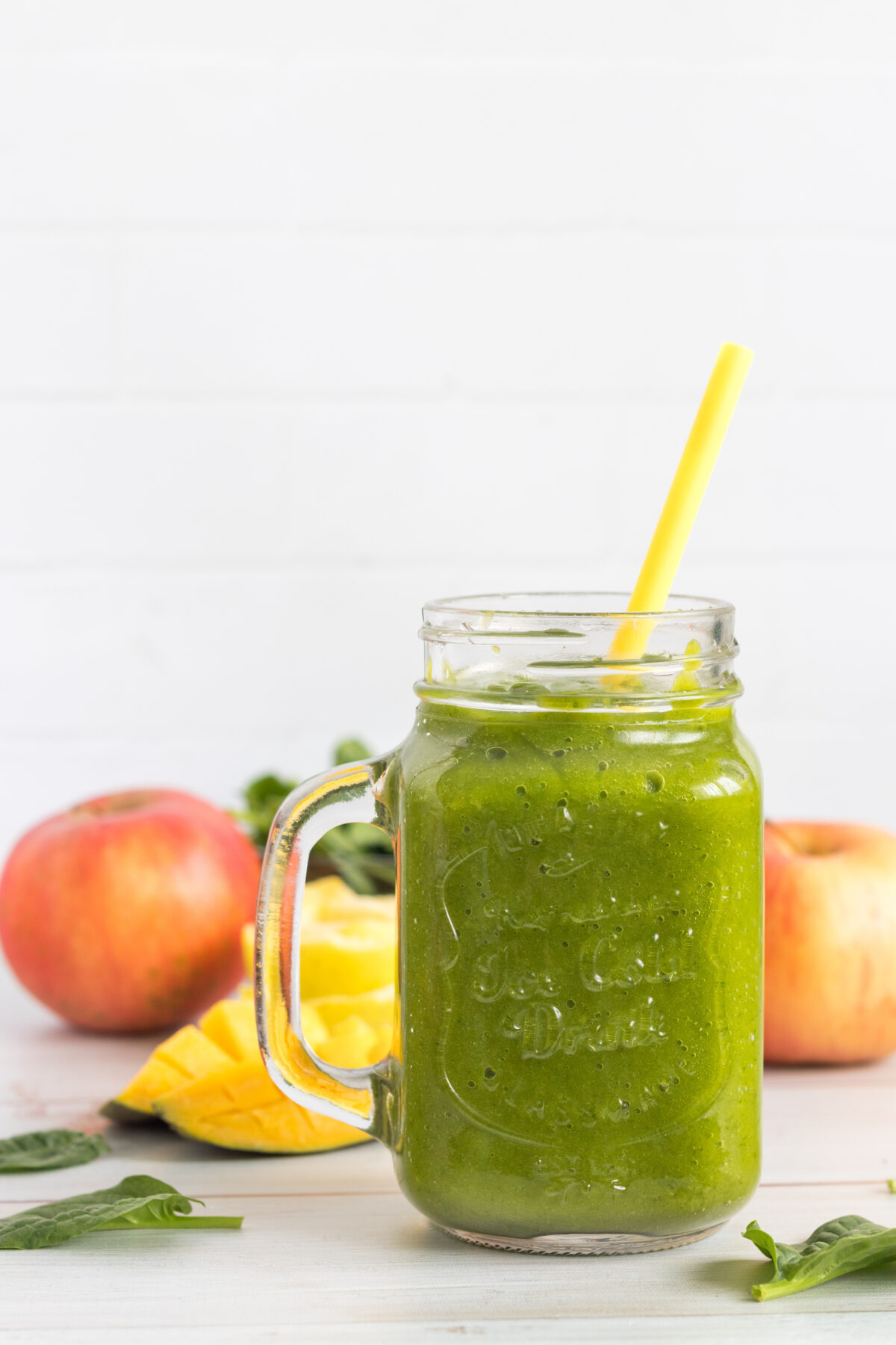 spinach mango apple smoothie in a mason jar glass with fresh produce in the background