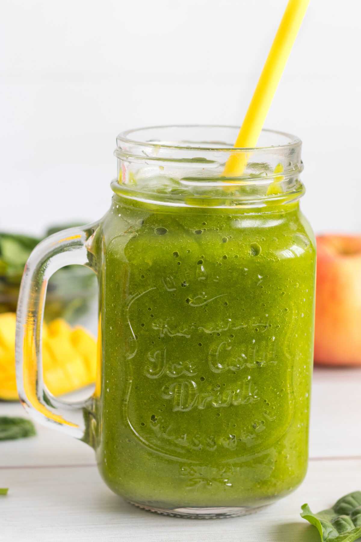 mango spinach smoothie in a glass with a jar