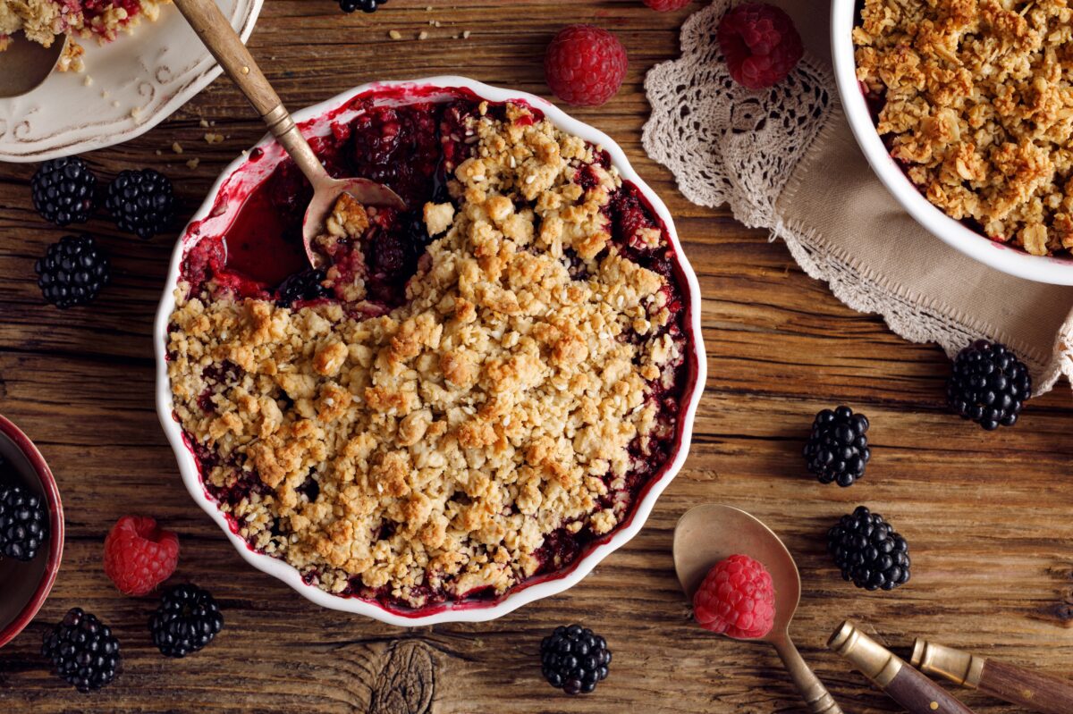 mixed berry crisp with a crumble topping in a ceramic baking dish with a spoon
