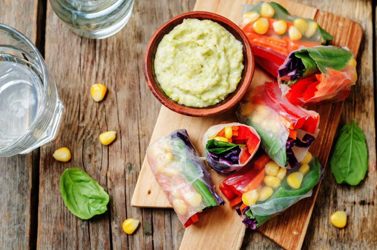 rainbow spring rolls with avocado white bean hummus on a dark wood background. 