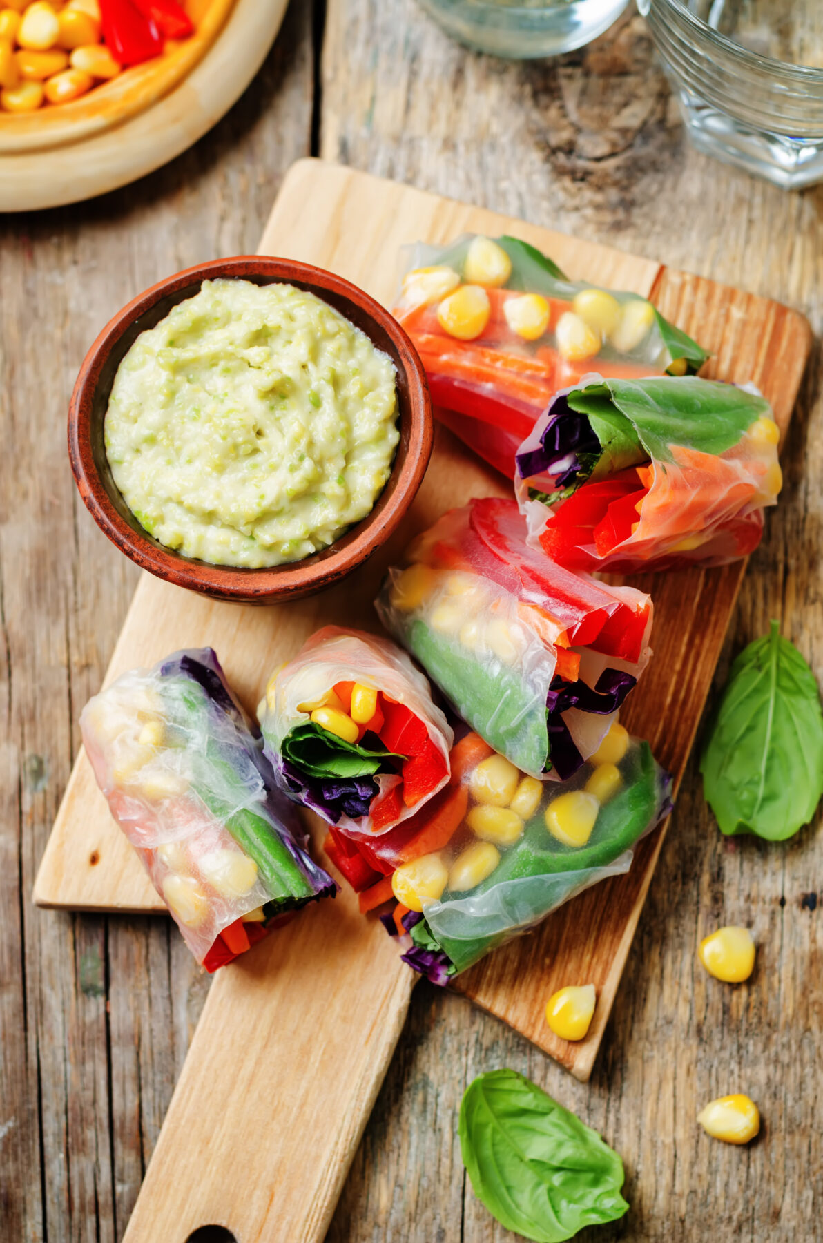 rainbow spring rolls with avocado white bean hummus on a dark wood background.