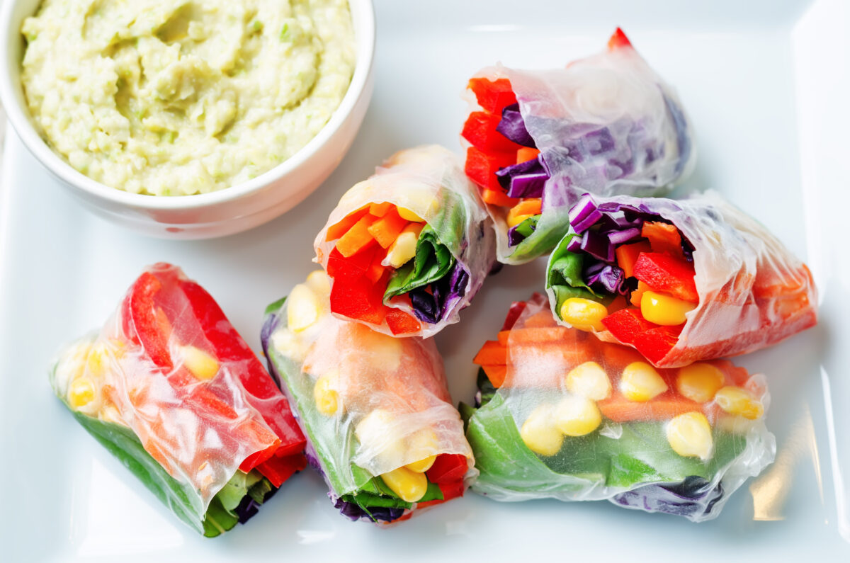 rainbow spring rolls with avocado white bean hummus on white wood background. 