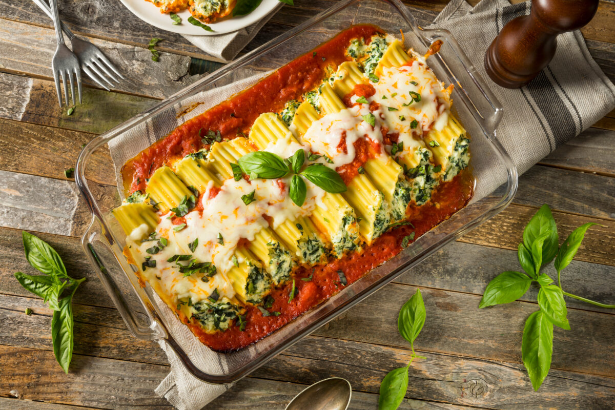 Homemade Stuffed Ricotta and Spinach Manicotti with Basil in a glass baking dish on a wooden table