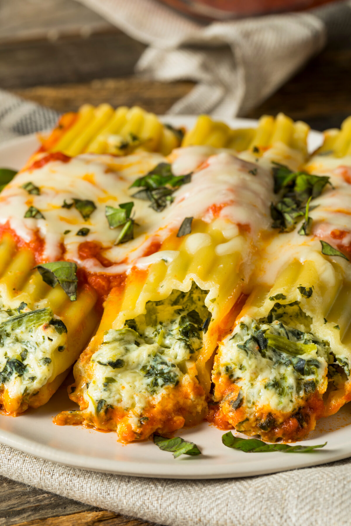 Homemade Stuffed Ricotta and Spinach Manicotti with Basil on a serving plate with a linen