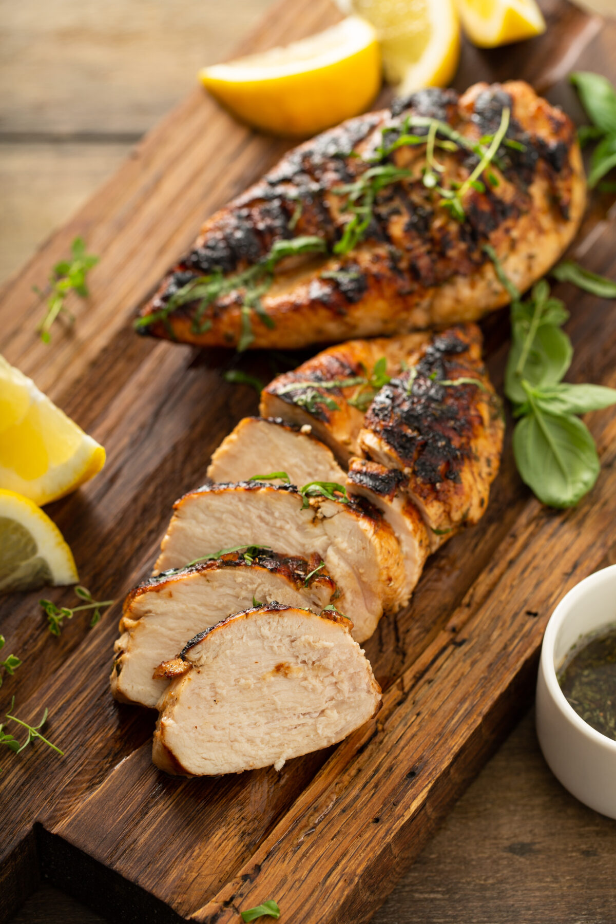 Balsamic grilled chicken breast with fresh herbs sliced on a rustic wooden board