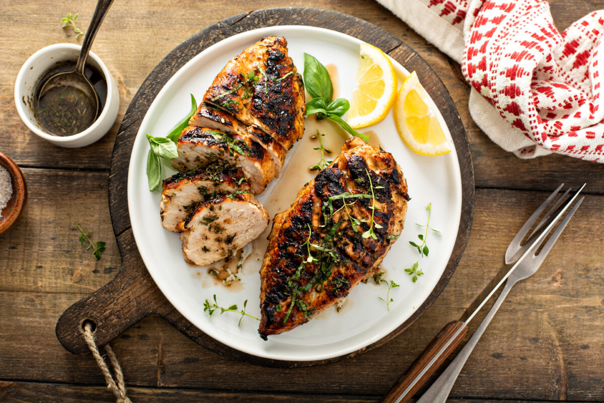 Balsamic grilled chicken breast with fresh herbs whole and sliced on a white plate