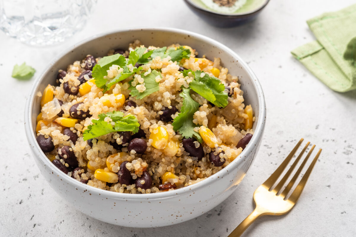 Two bowls contain quinoa salad mixed with black beans and corn, garnished with cilantro. These bowls are placed on a light table during a casual lunch setting.