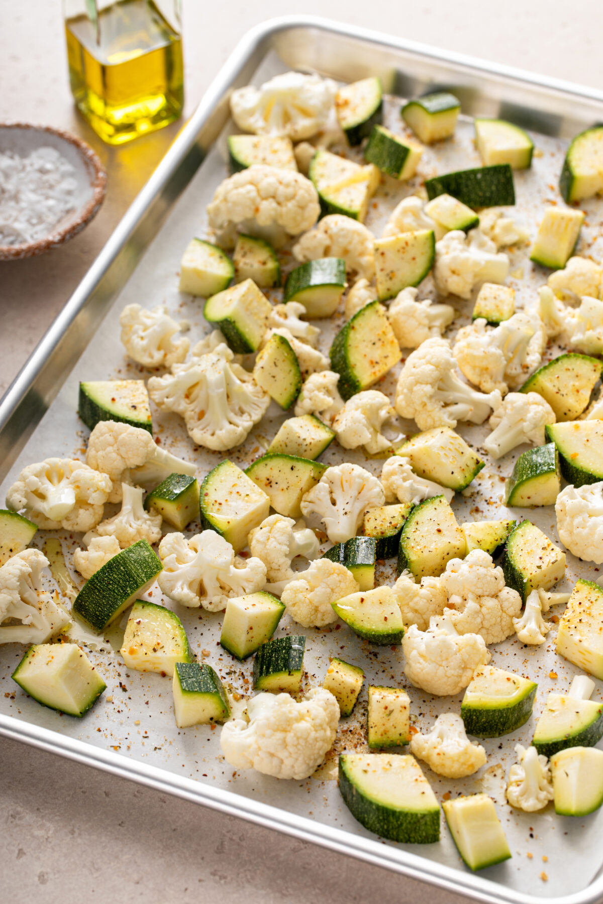 Fresh cauliflower and zucchini chopped on a baking sheet ready to be roasted with garlic and herbs
