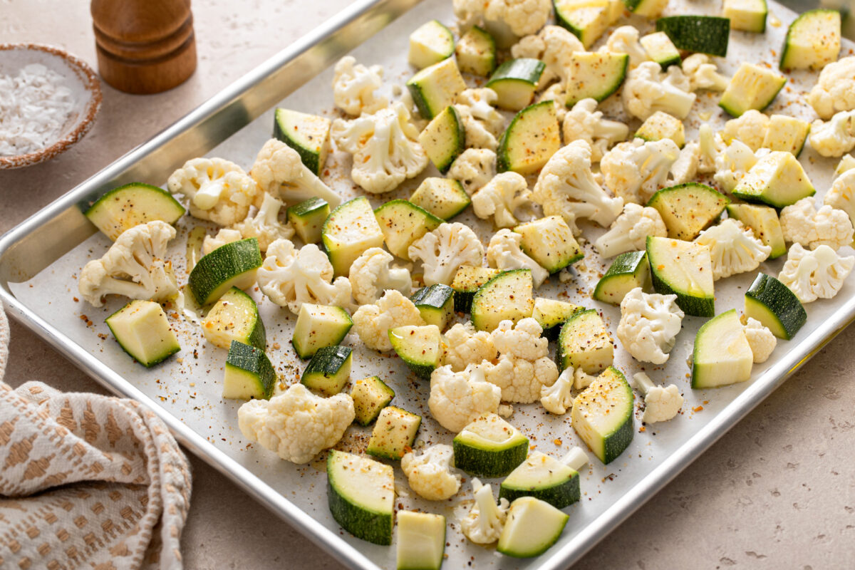 Fresh cauliflower and zucchini chopped on a baking sheet ready to be roasted with garlic and herbs