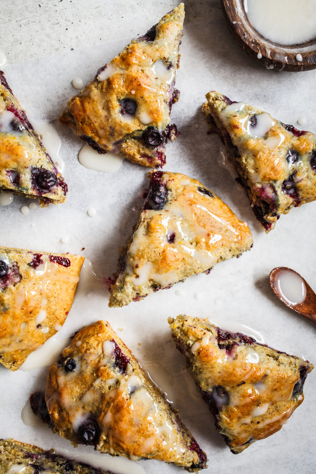 blueberry scones cut into wedges and drizzled with icing on a sheet of parchment paper