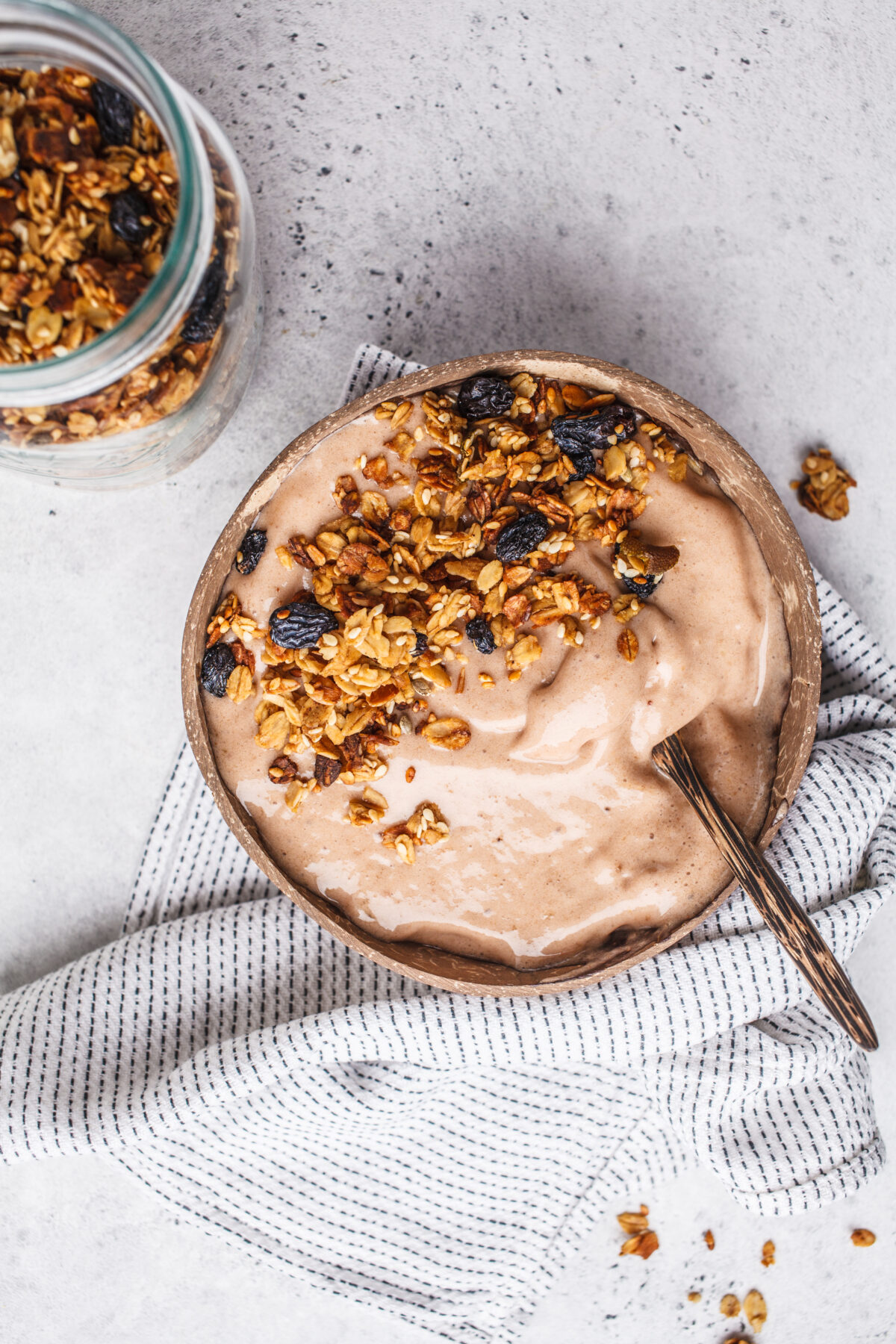 Chocolate smoothie bowl with granola in a coconut bowl, top view with a striped linen