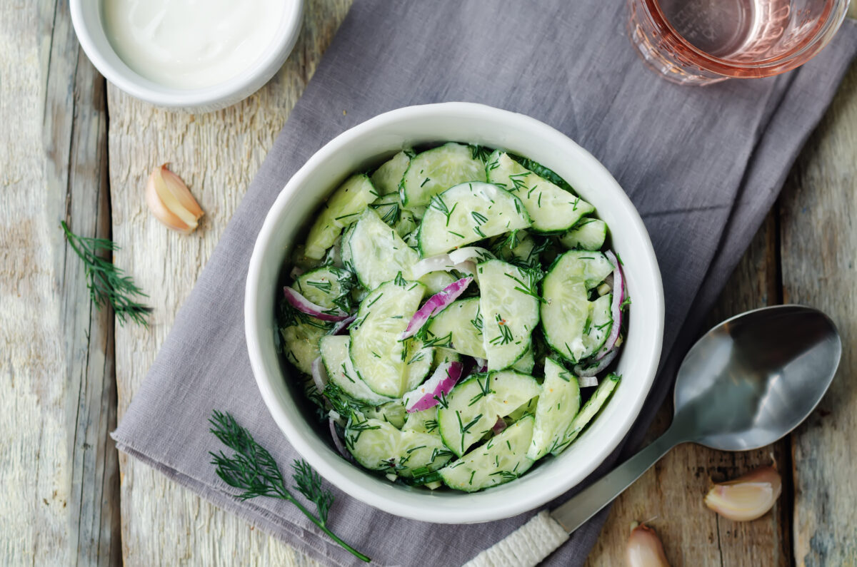 Greek yogurt red onion cucumber salad in a serving bowl on a wooden table.