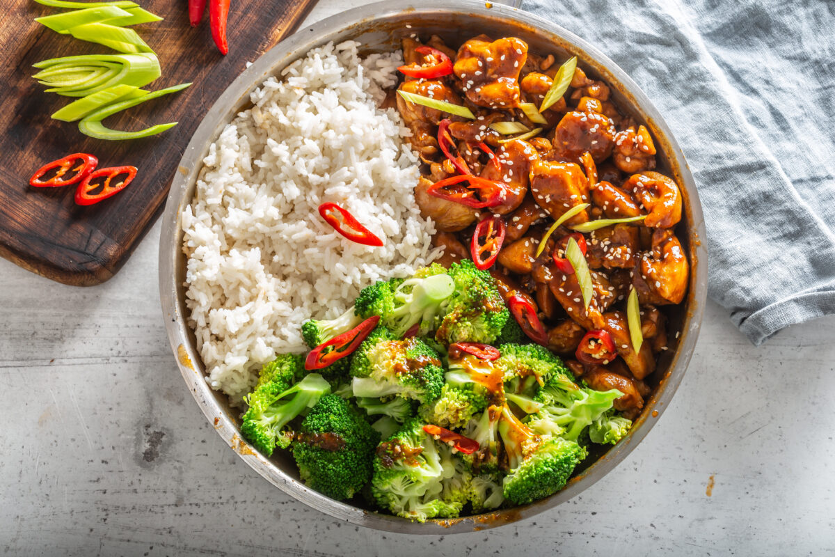 teriyaki chicken with rice, broccoli and chili on a white table.