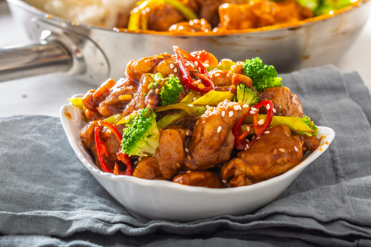 Bowl of teriyaki chicken sprinkled with sesame seeds, fresh chillies and broccoli.