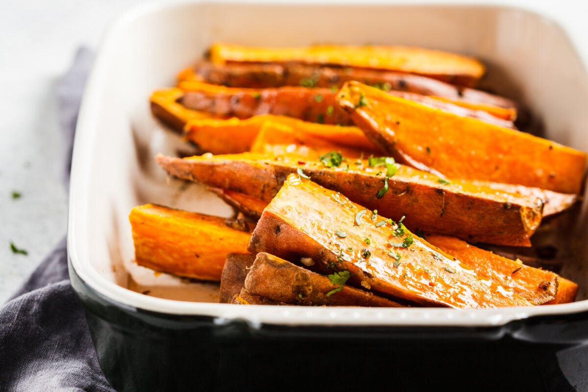Baked sweet potato slices with spices in oven dish.