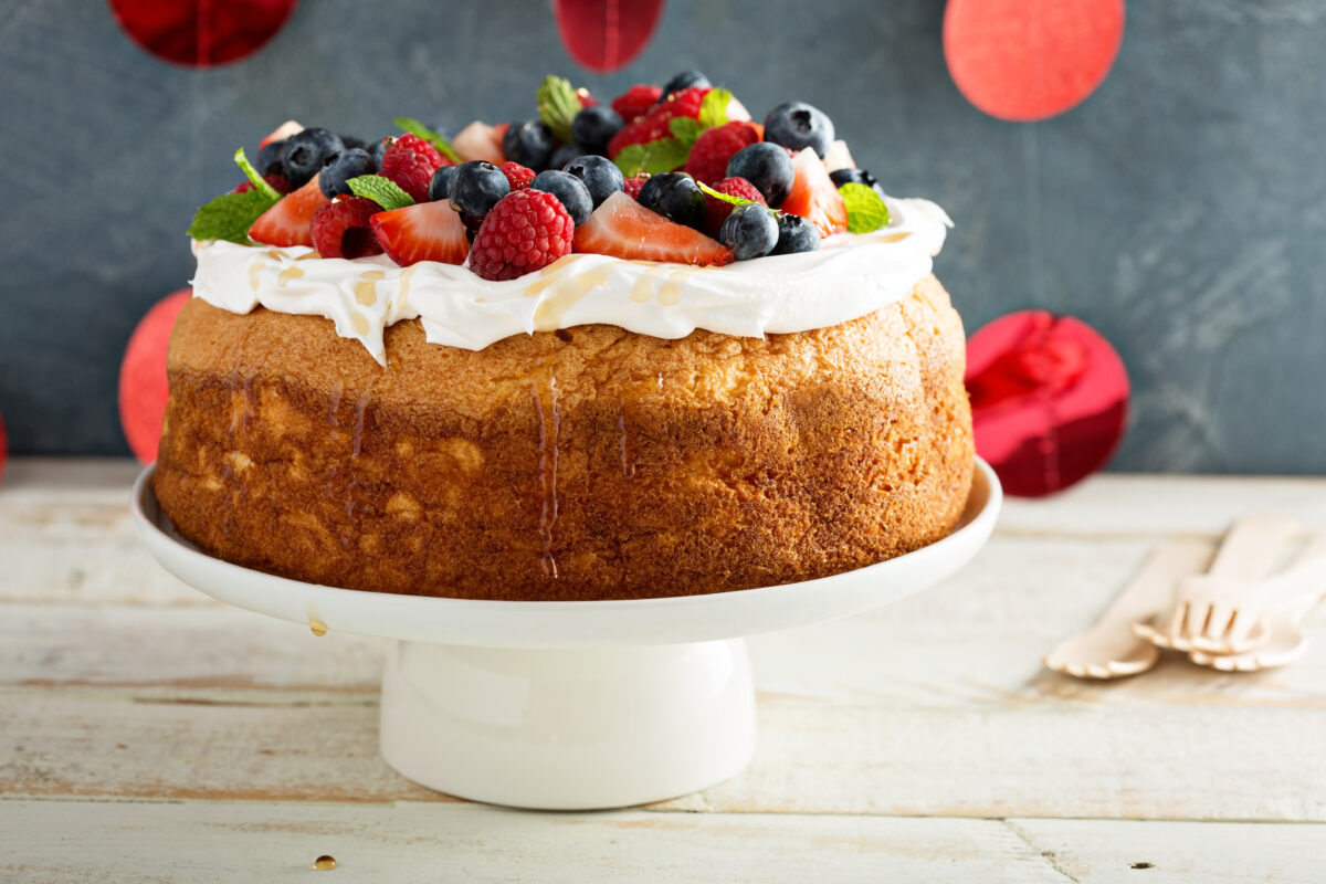 Angel food cake with whipped cream and fresh berries on a white pedestal