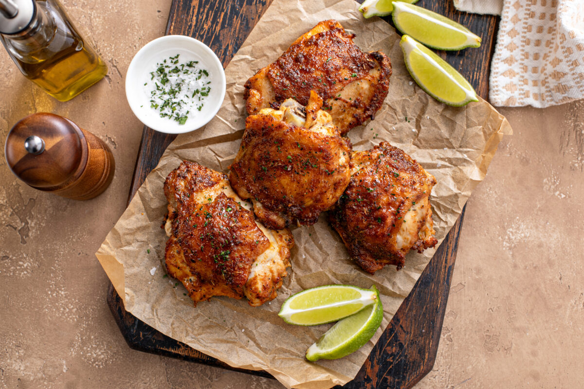 Chicken thighs roasted or air fried with paprika, spices rub and lime on a cutting board