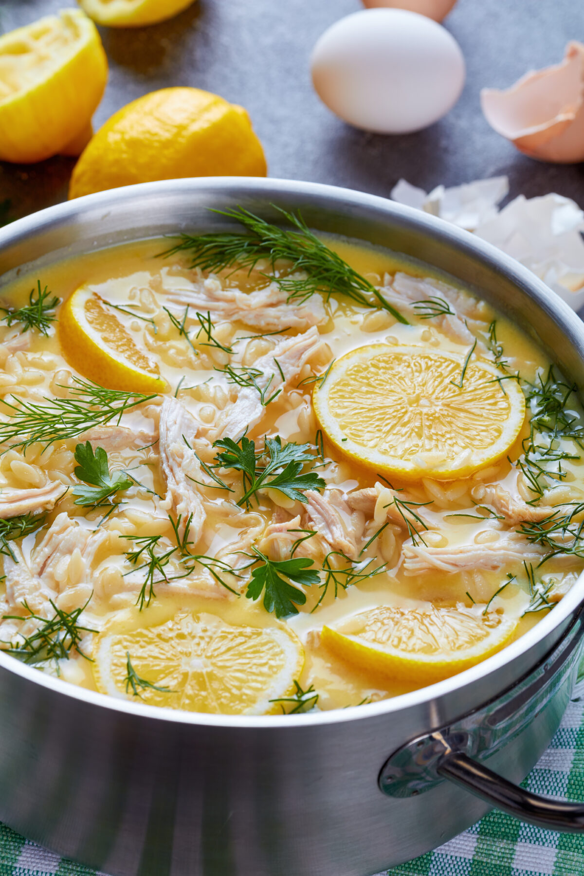 avgolemono - delicious creamy greek chicken soup with lemon and herbs in a casserole on a concrete table with ingredients at the background, view from above