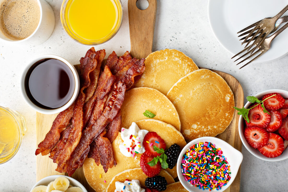 a fun breakfast board with pancakes, fresh fruit, crispy bacon, syrup and sprinkles