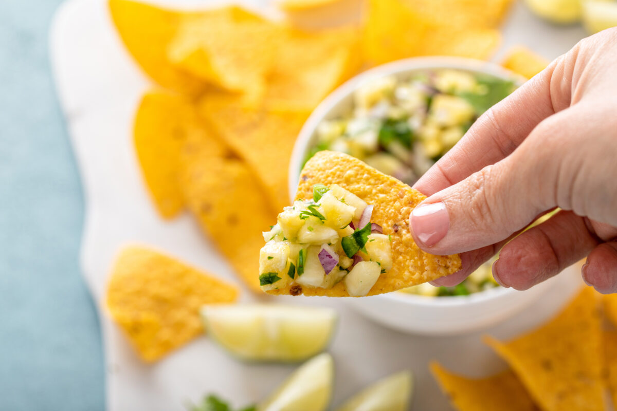 Pineapple salsa with jalapeno, cilantro and red onion served with corn chips, scooping up salsa with a chip