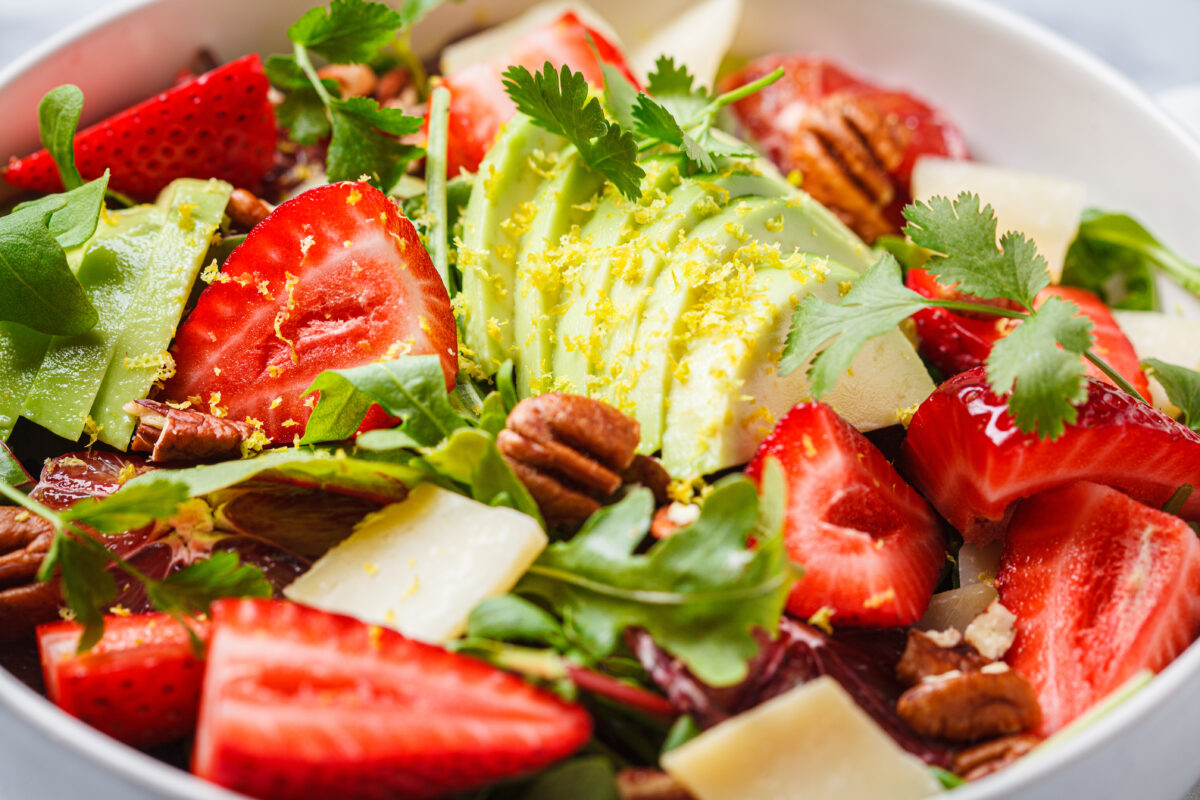 Strawberry and avocado salad with arugula, parmesan, nuts and lemon zest, close-up. 