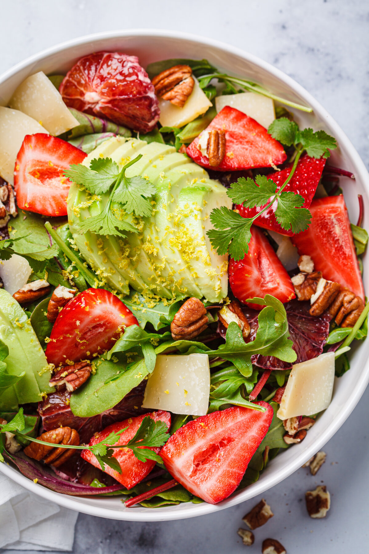 Strawberry and avocado salad with arugula, parmesan, nuts and lemon zest, close-up. Summer salad recipe.