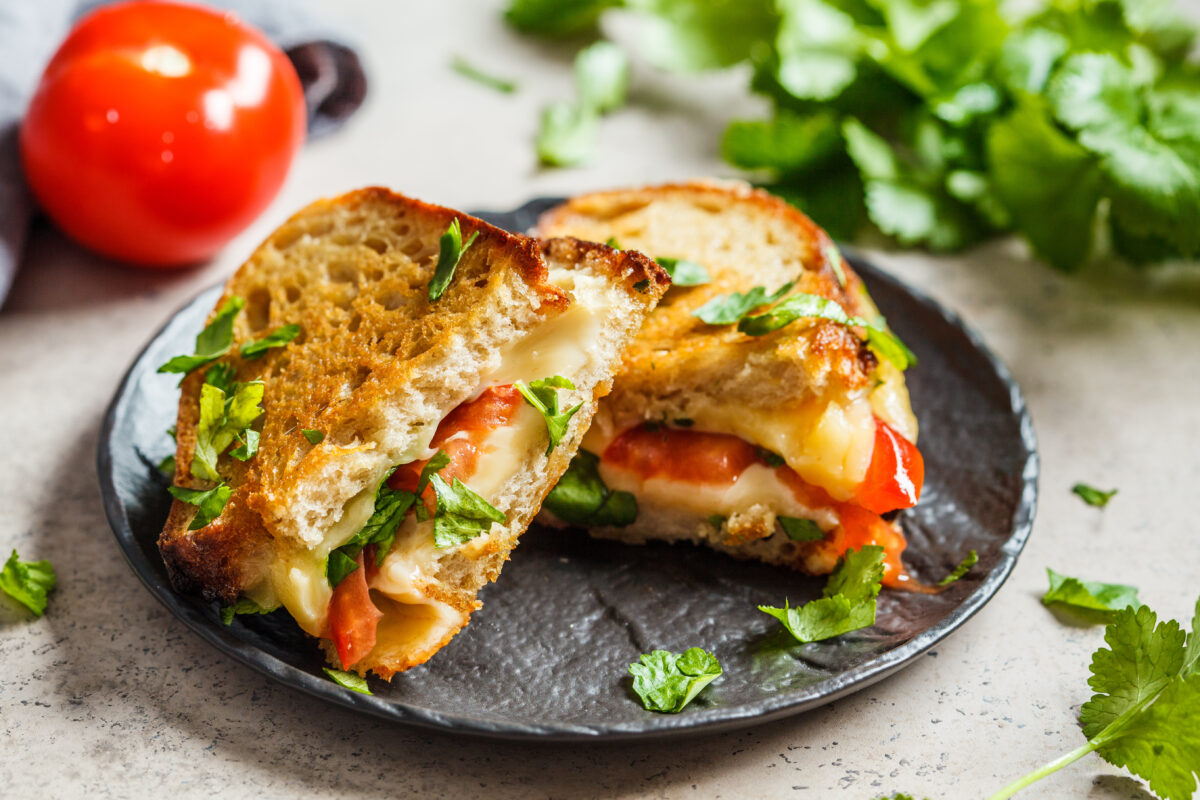 Grilled cheese sandwich with tomato and herbs, dark background.