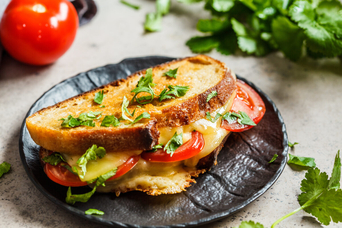 caprese grilled cheese sandwich with fresh tomato and basil on a dark plate