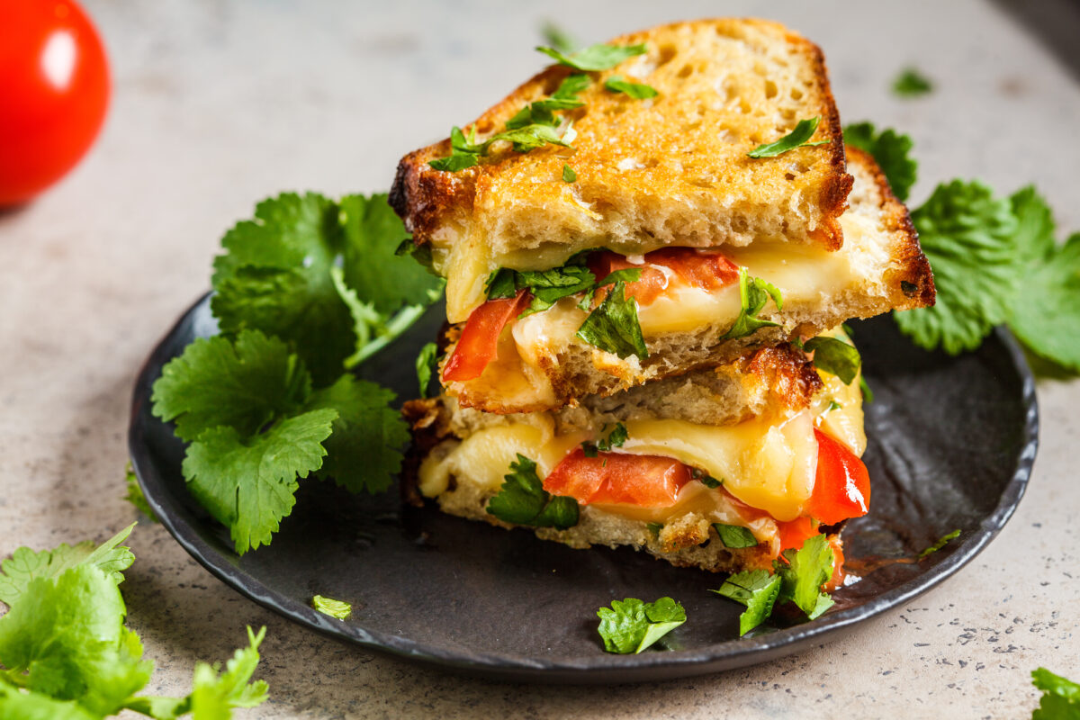 caprese grilled cheese with fresh tomatoes and greens on a dark plate