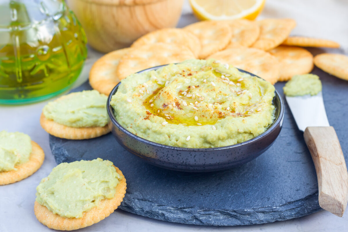 Healthy avocado hummus sprinkled with olive oil, paprika and sesame, served with crackers.