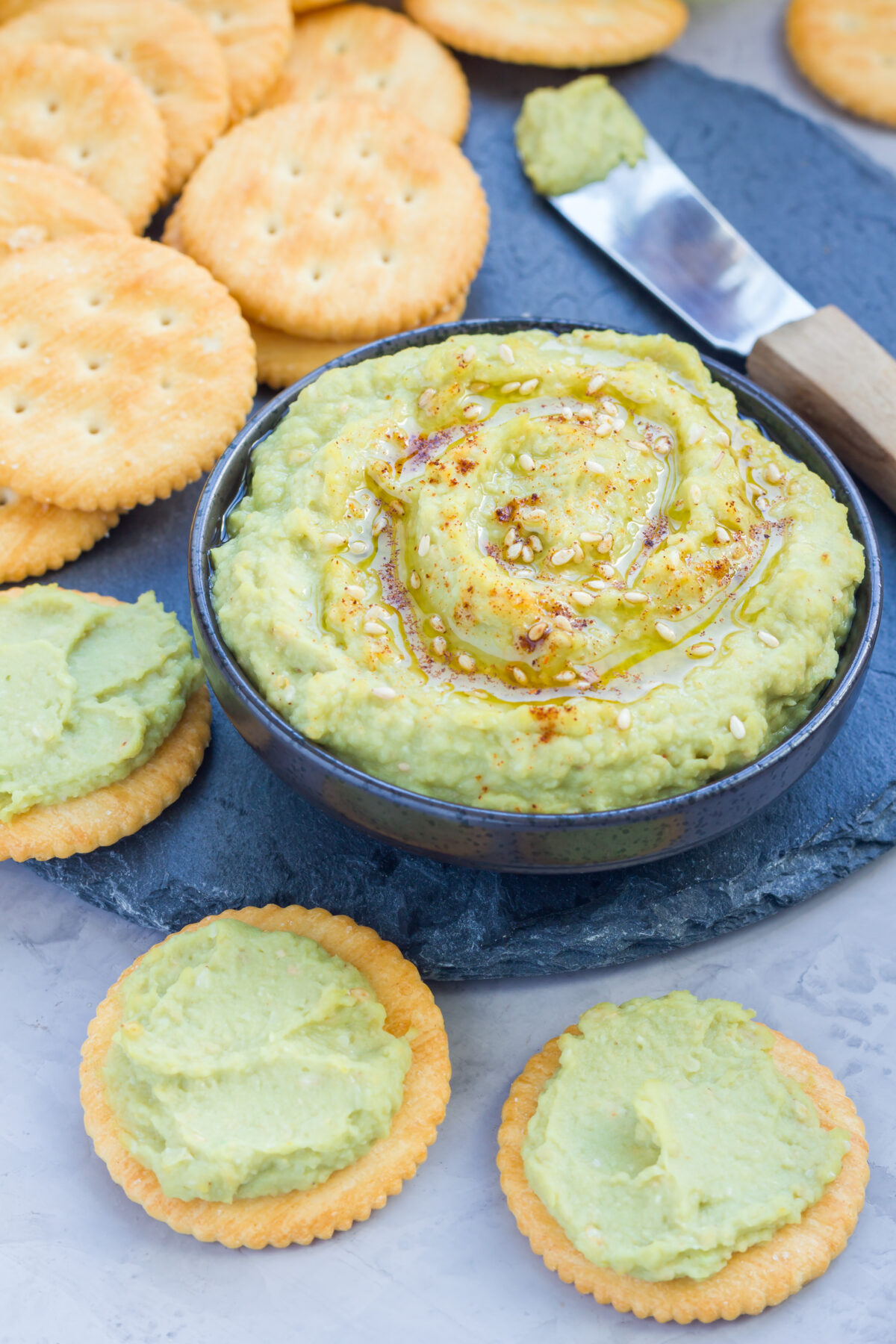 Healthy avocado hummus sprinkled with olive oil, paprika and sesame, served with crackers.