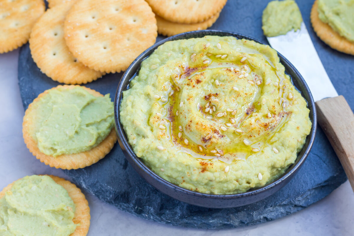 Healthy avocado hummus sprinkled with olive oil, paprika and sesame, served with crackers.