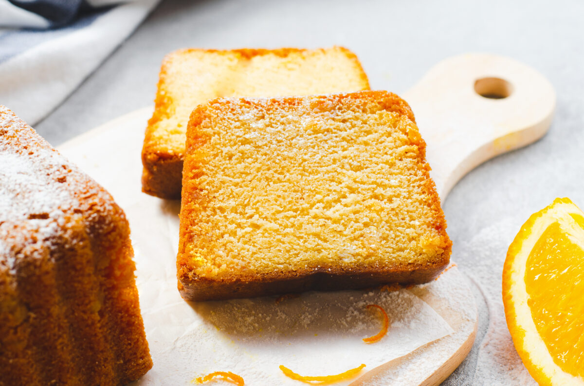 Orange pound cake cut into slices with powdered sugar on a wooden board