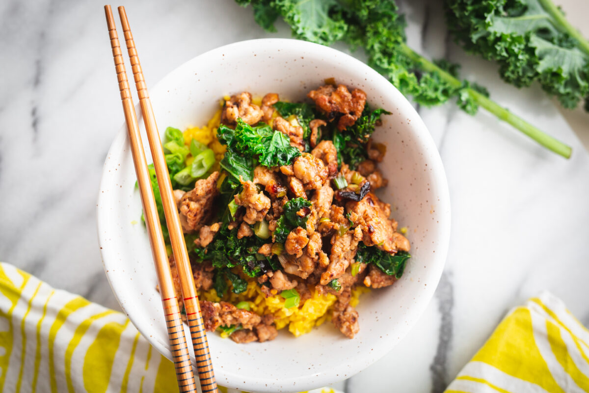 Pork and kale bowl with yellow rice in serving bowl with chopsticks
