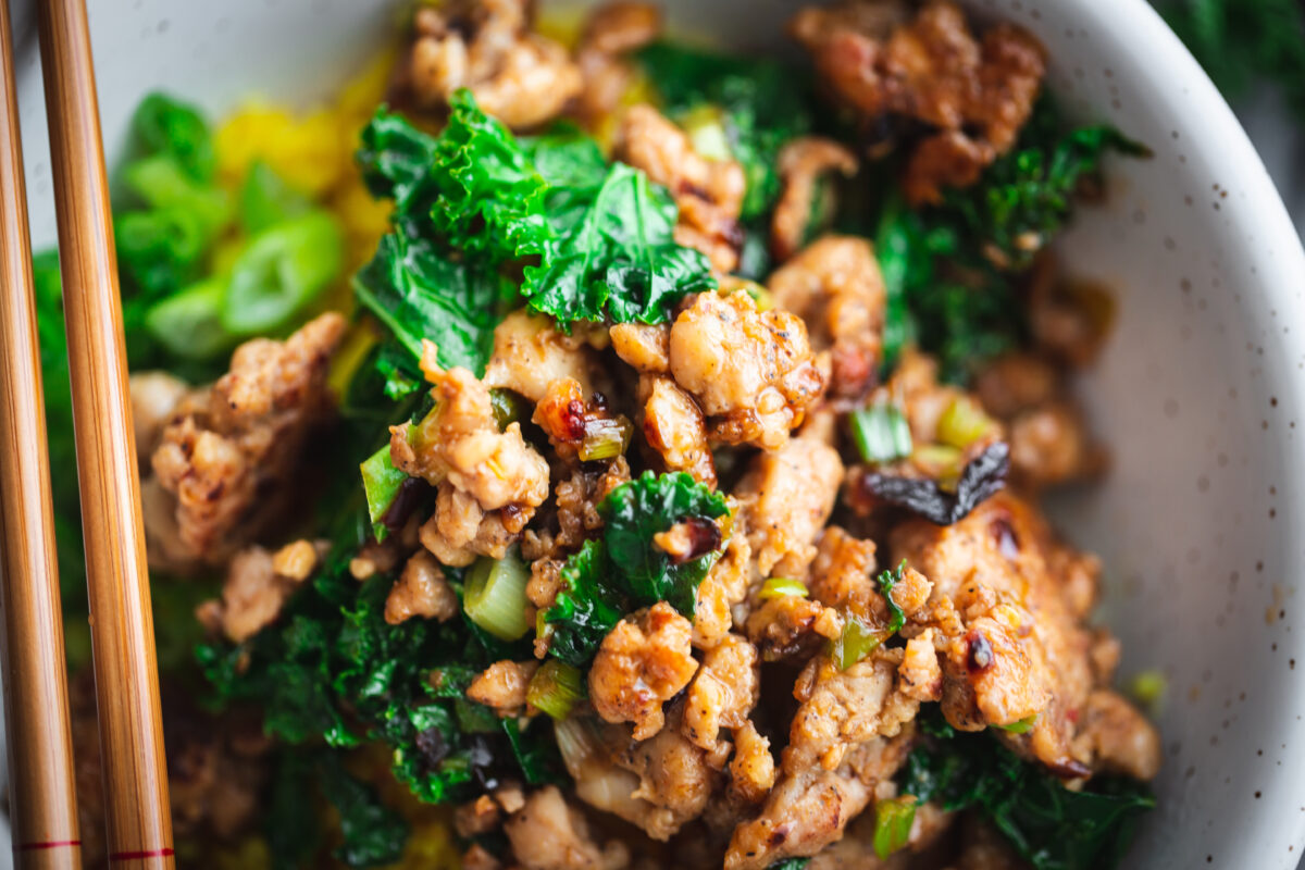 a close up picture of pork and kale bowl with chopsticks in a serving bowl