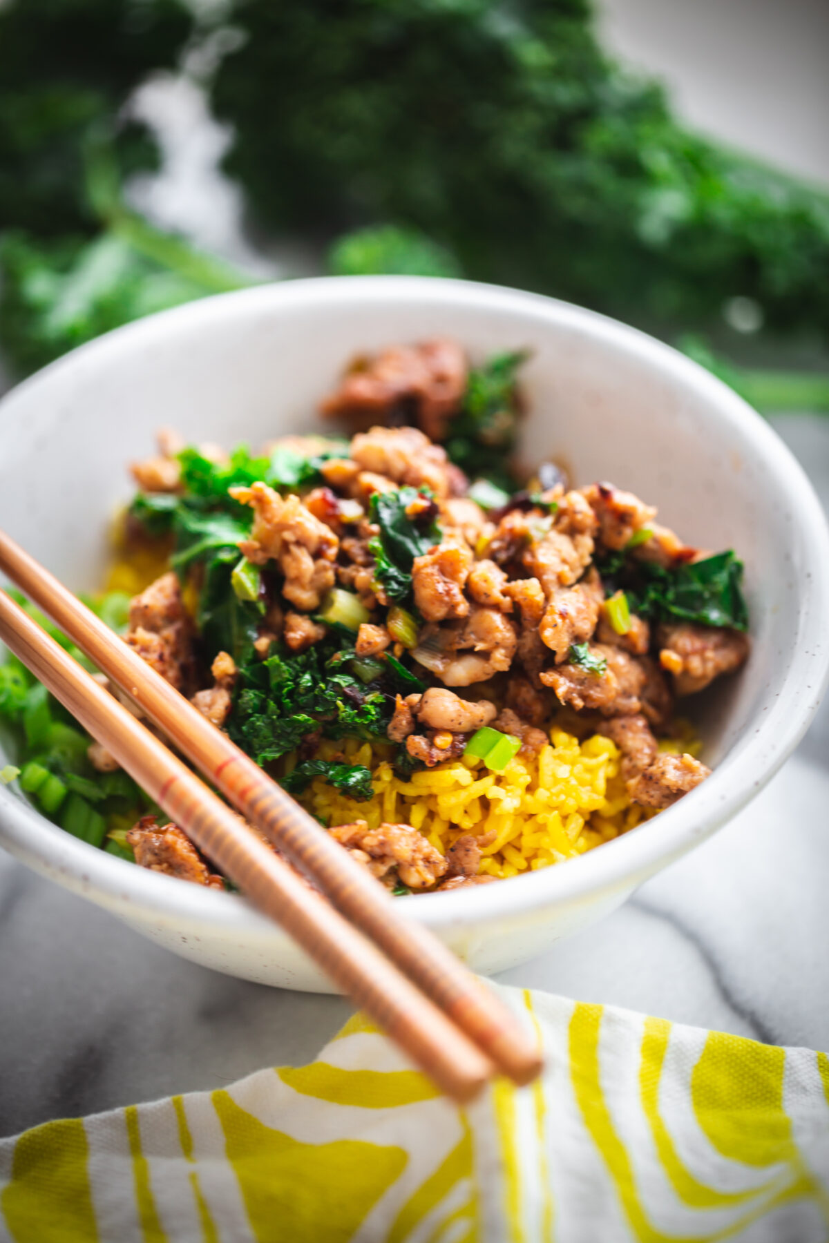pork and kale over yellow rice in a serving bowl with chopsticks