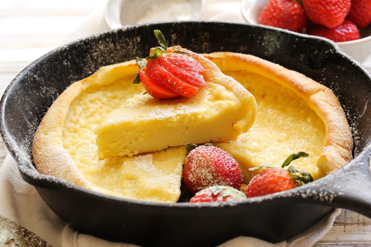 Dutch baby Puffed Pancake baked in cast iron skillet topped with strawberries and powdered sugar