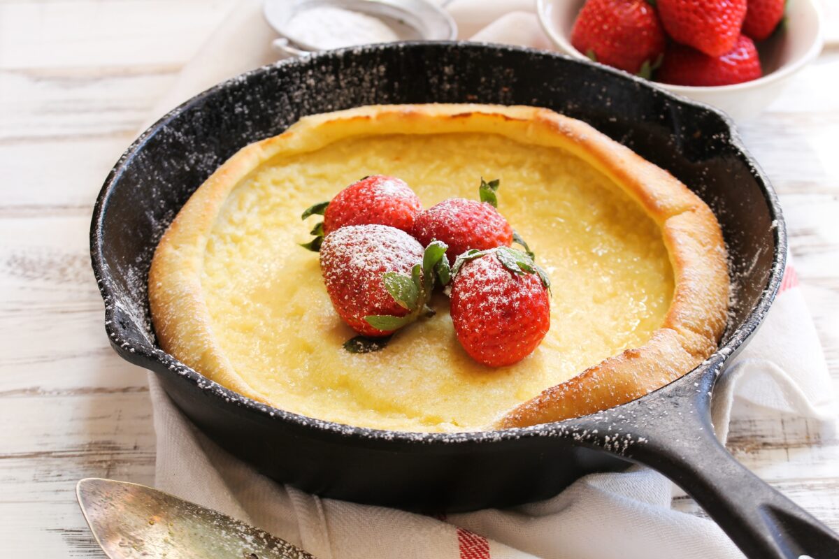 Dutch baby Puffed Pancake baked in cast iron skillet with strawberries and a striped linen