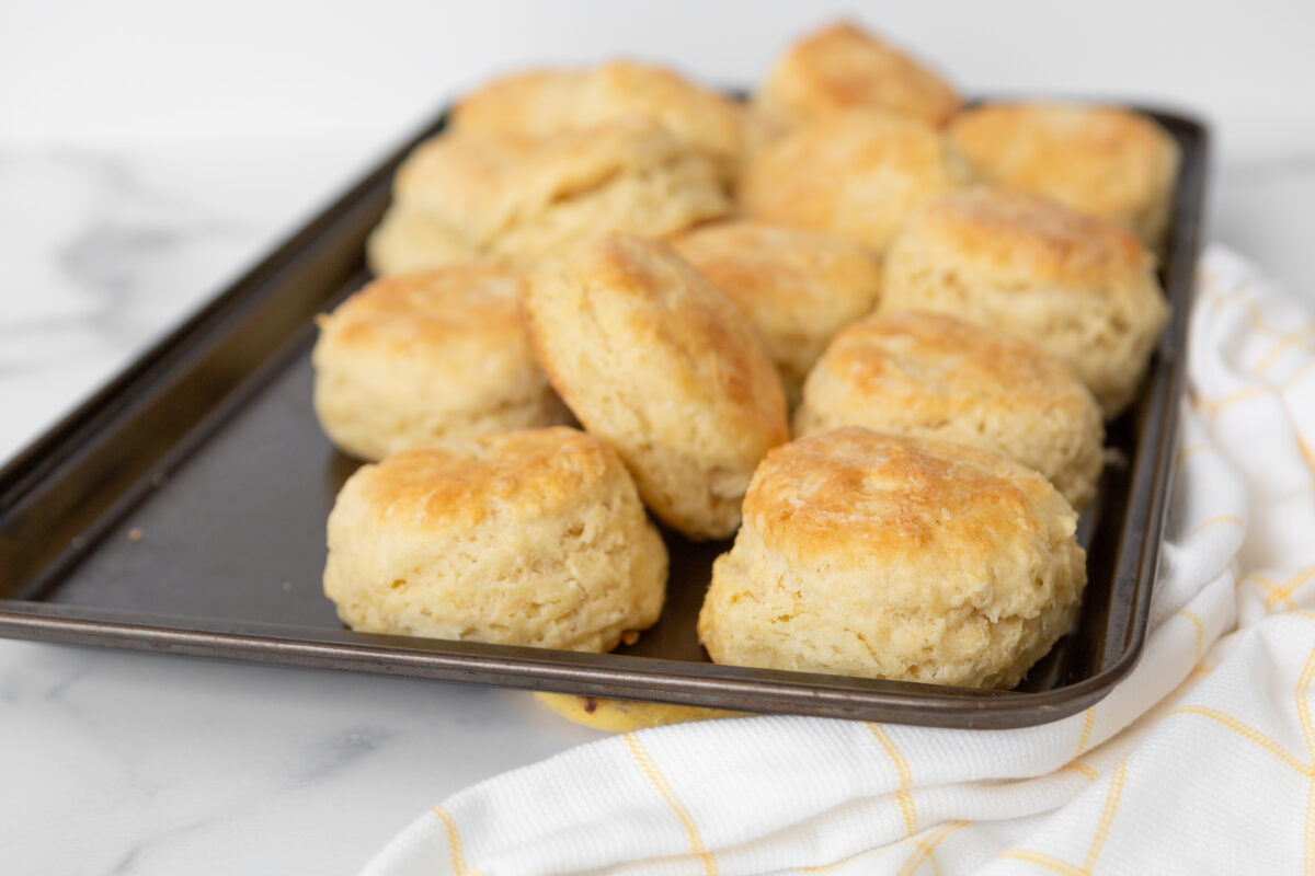 freshly baked fluffy buttermilk biscuits on a sheet pan with a plaid linen