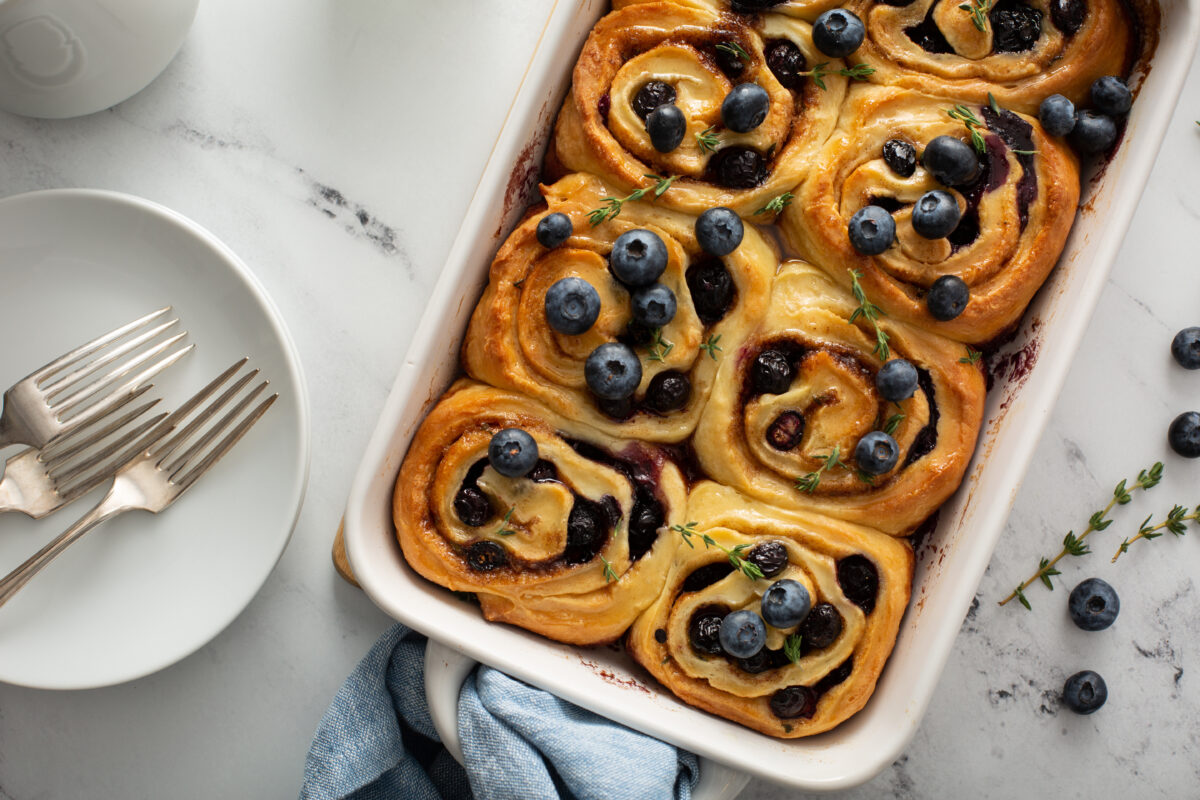 fresh blueberry rolls in a white baking dish with serving forks