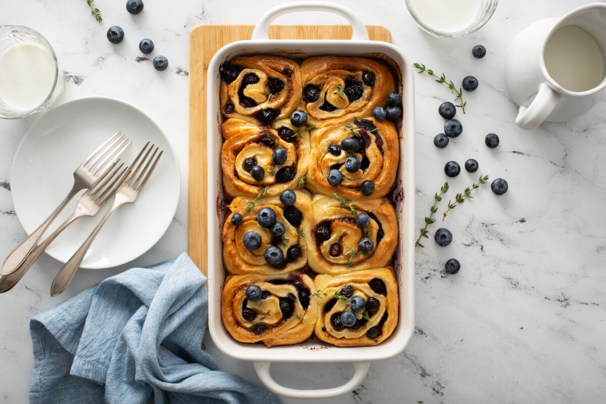 blueberry rolls with fresh thyme in a baking dish with serving plates and blue linen