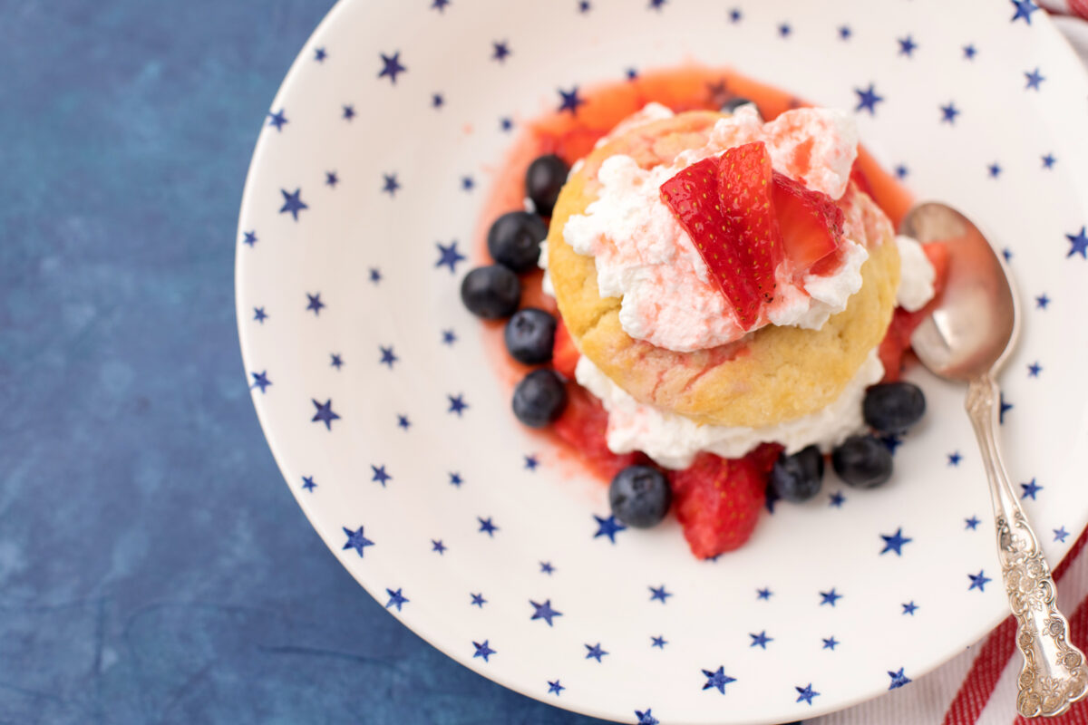 an overhead shot of shortcake with whipped cream, strawberries and blueberries on a star decorated plate