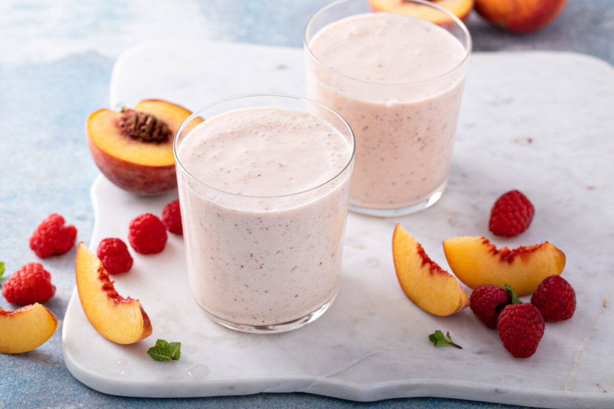 Raspberry peach smoothie in small glasses, with fresh peaches and raspberries