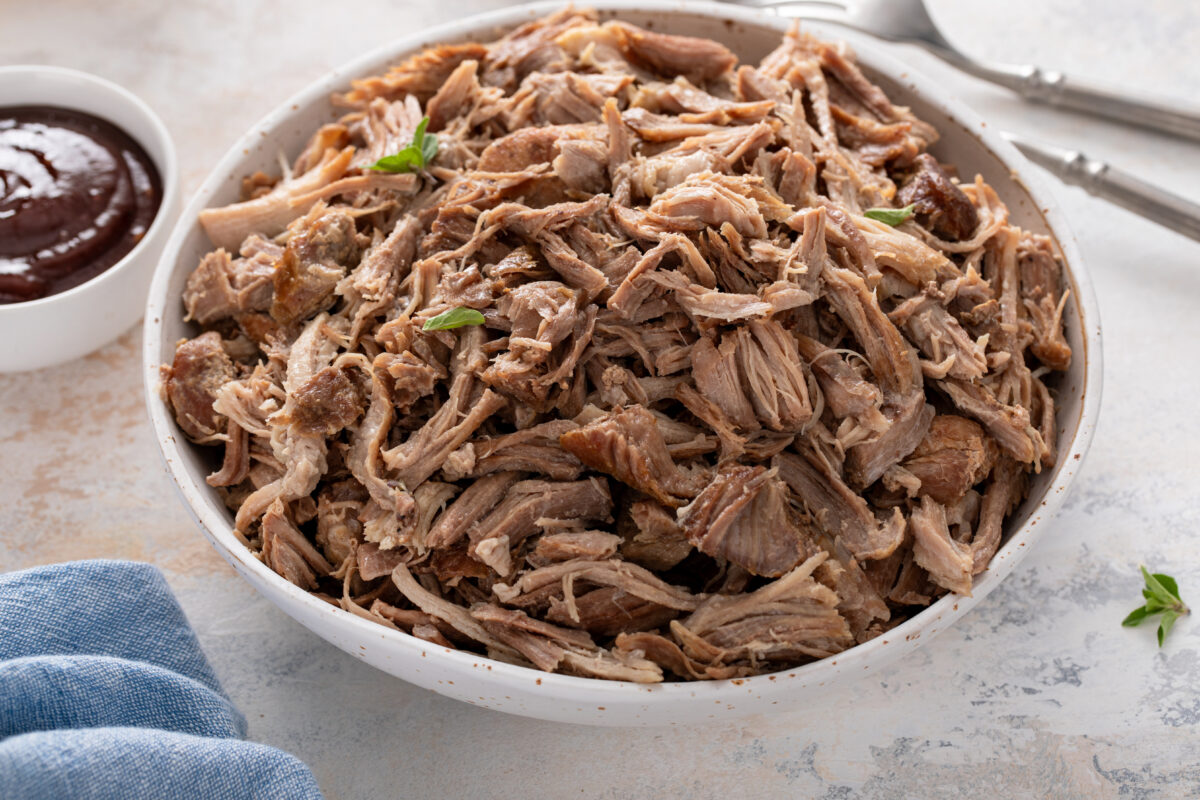 Pulled pork or carnitas cooked in a slow cooker served in a bowl to make sandwiches with brioche buns and cabbage