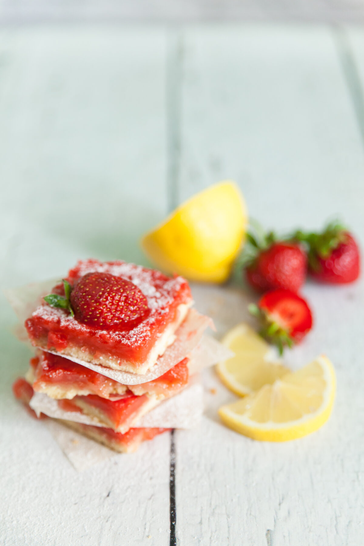 strawberry lemon bars with a shortbread crust cut into squares and stacked with parchment paper