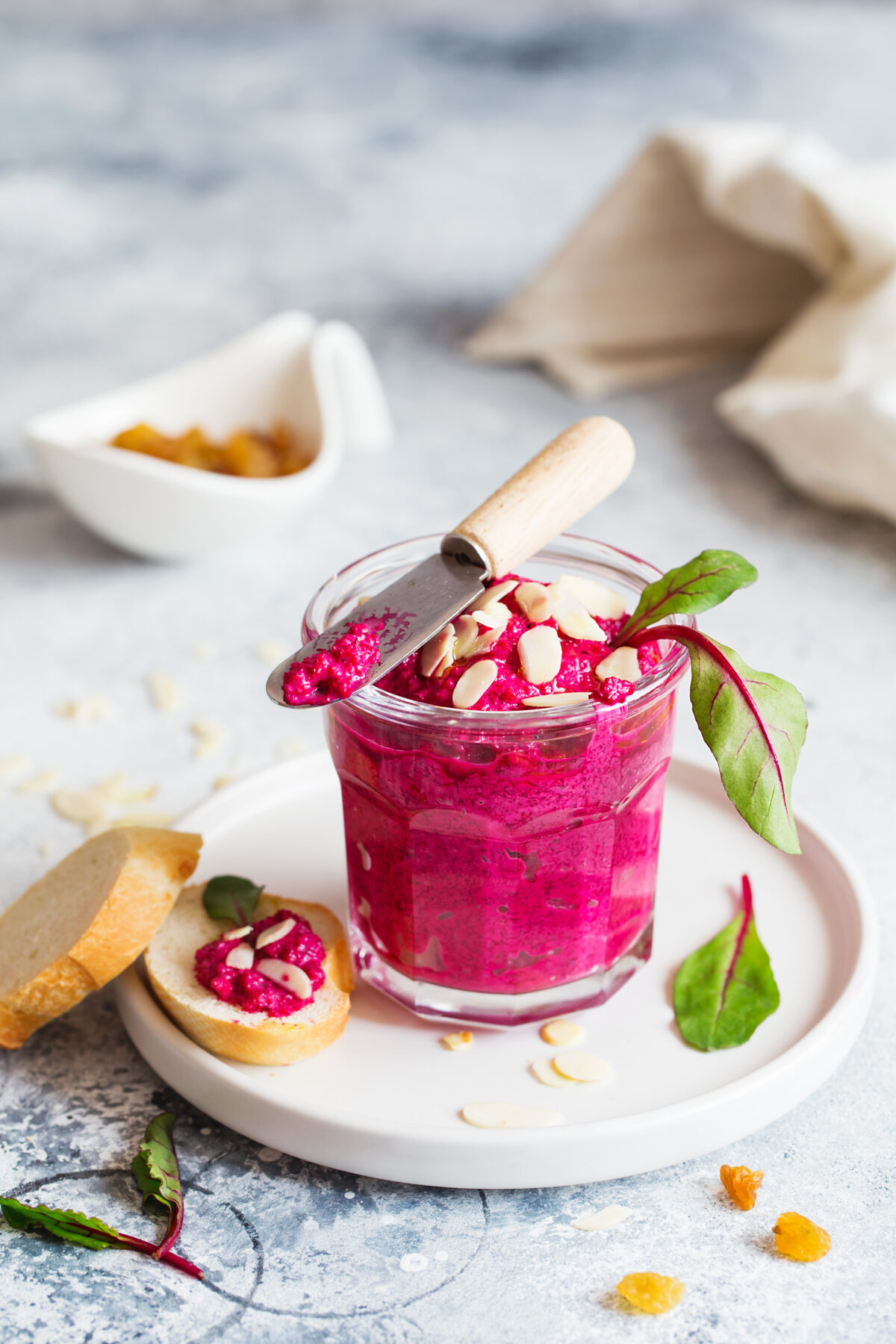 roasted beet hummus in a glass jar with almonds and fresh beet greens