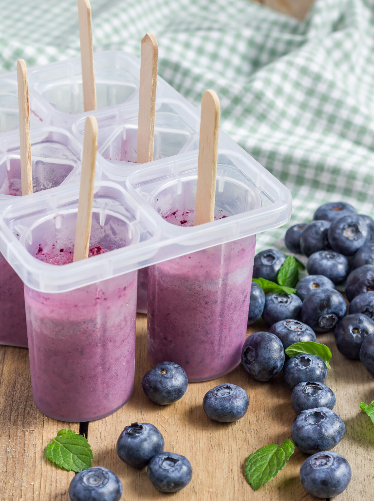 Blueberry protein popsicles in a mold with fresh blueberries and mint leaves