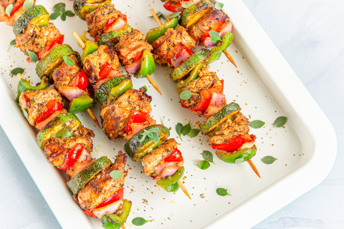 chicken and veggie kabobs with fresh herbs on a white platter