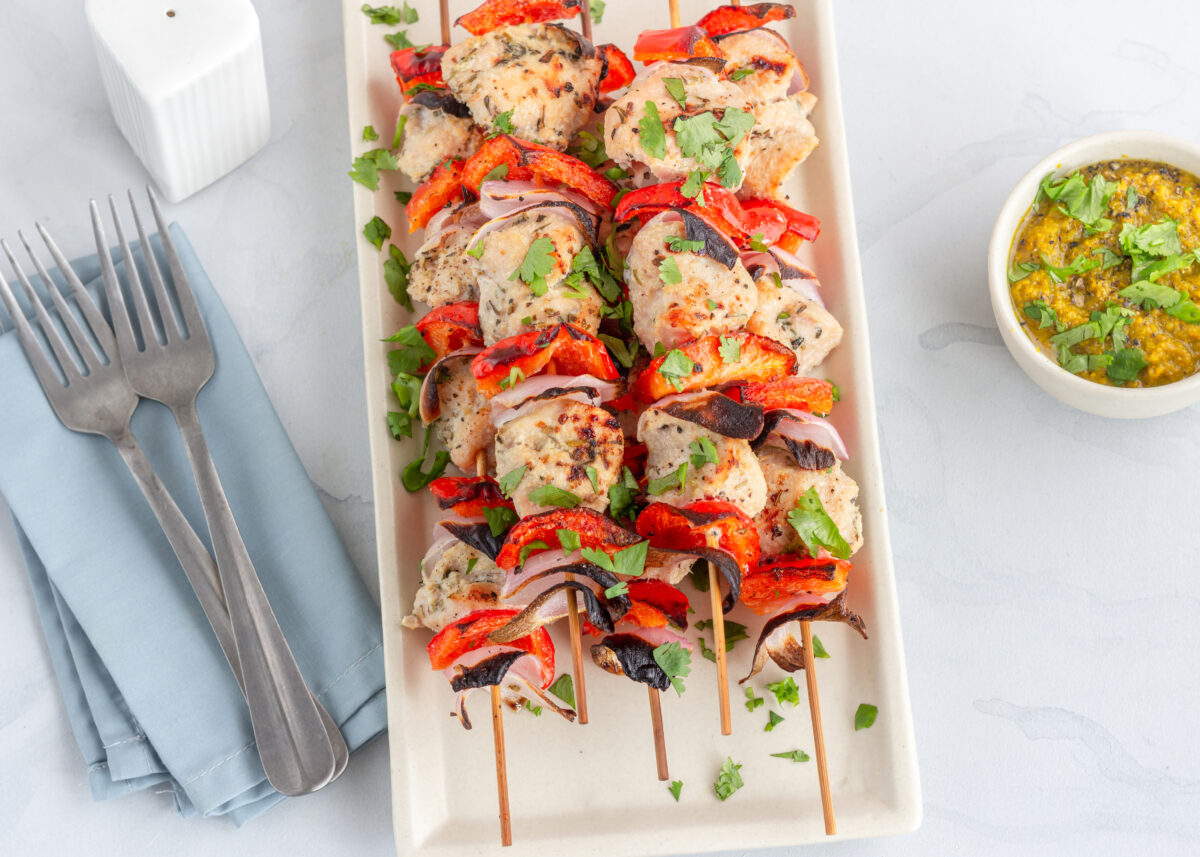 chicken kabobs on wooden skewers with a blue linen and fresh herbs